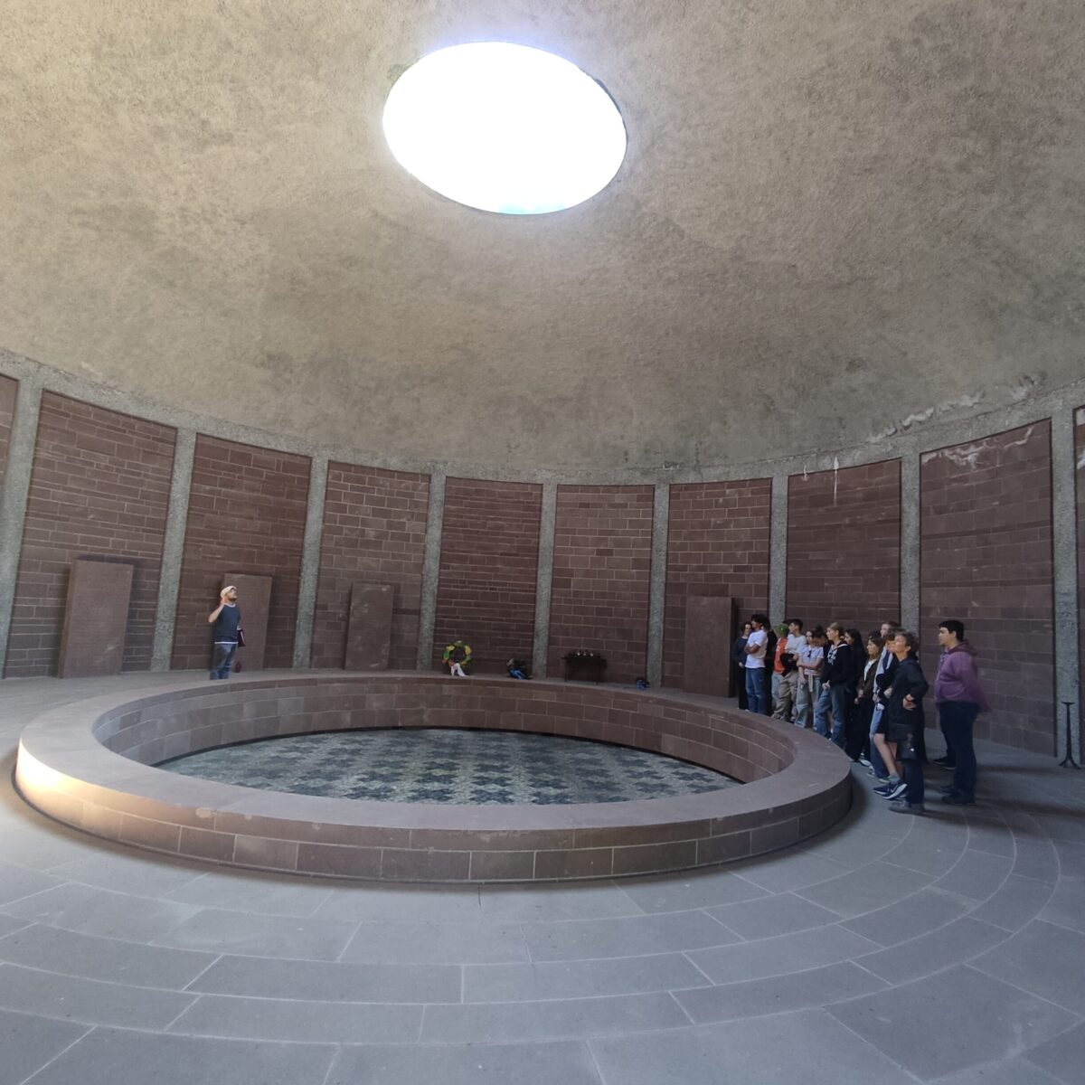 Große, runde Kuppelhalle mit zentralem Brunnen. Menschen stehen rechts, Blick nach innen gerichtet.