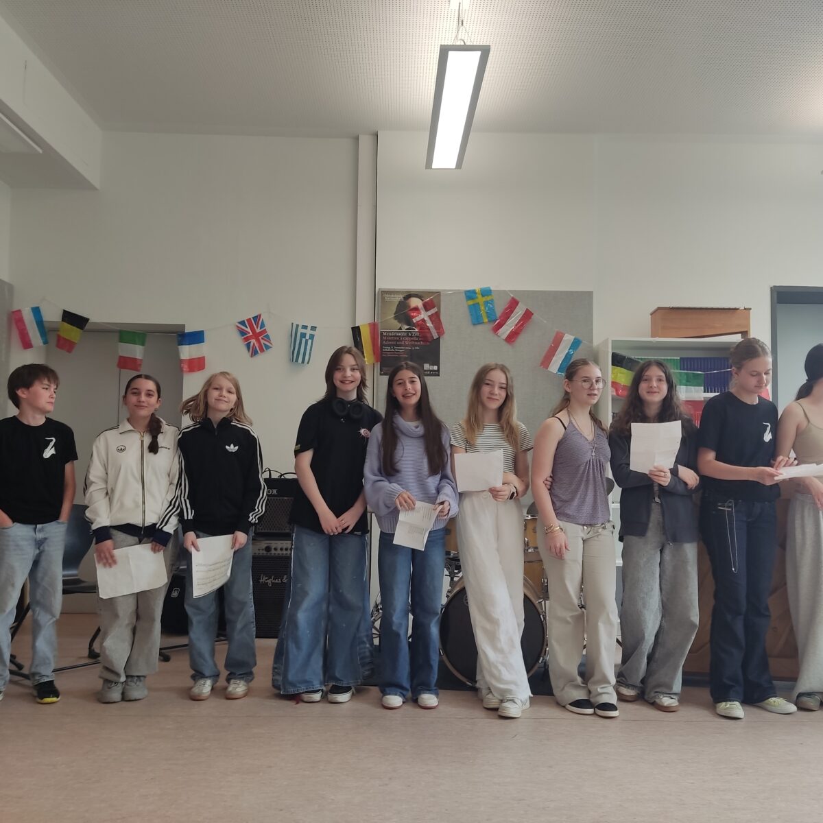 Eine Gruppe junger Menschen lächelt in einem Raum mit internationalen Flaggen.