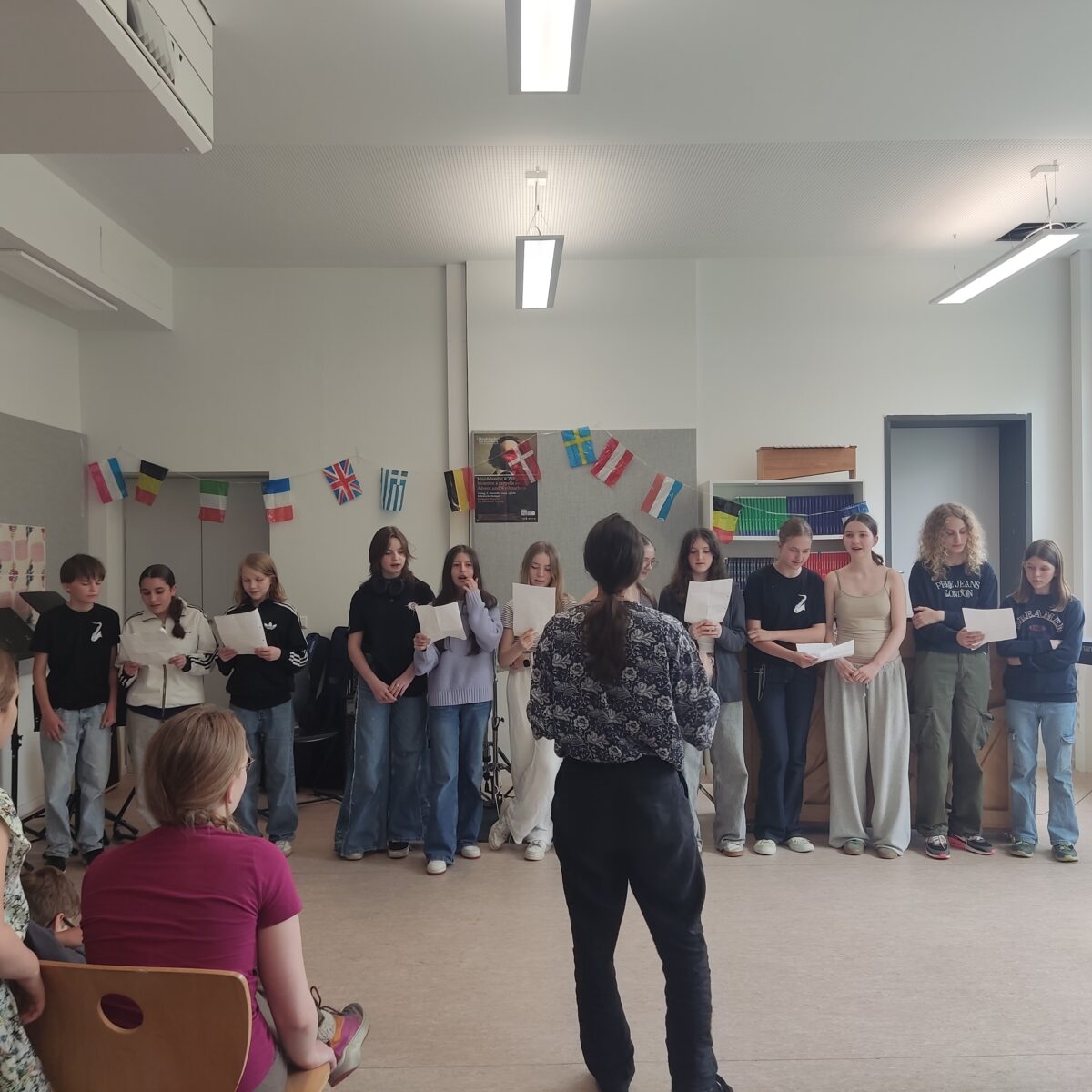 Gruppe von Jugendlichen präsentiert vor Publikum. Raum mit Flaggen dekoriert.