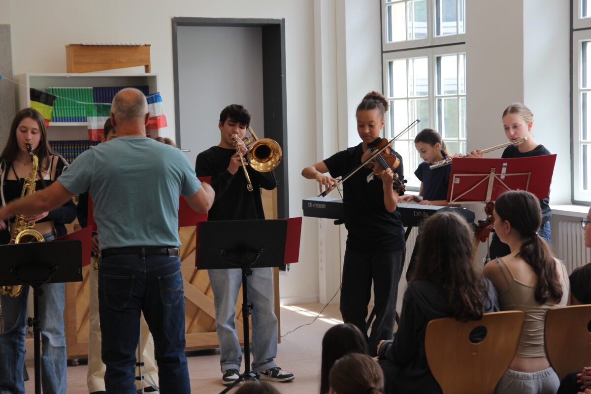 Ein Mann dirigiert eine Gruppe junger Musiker in einem Klassenraum.
