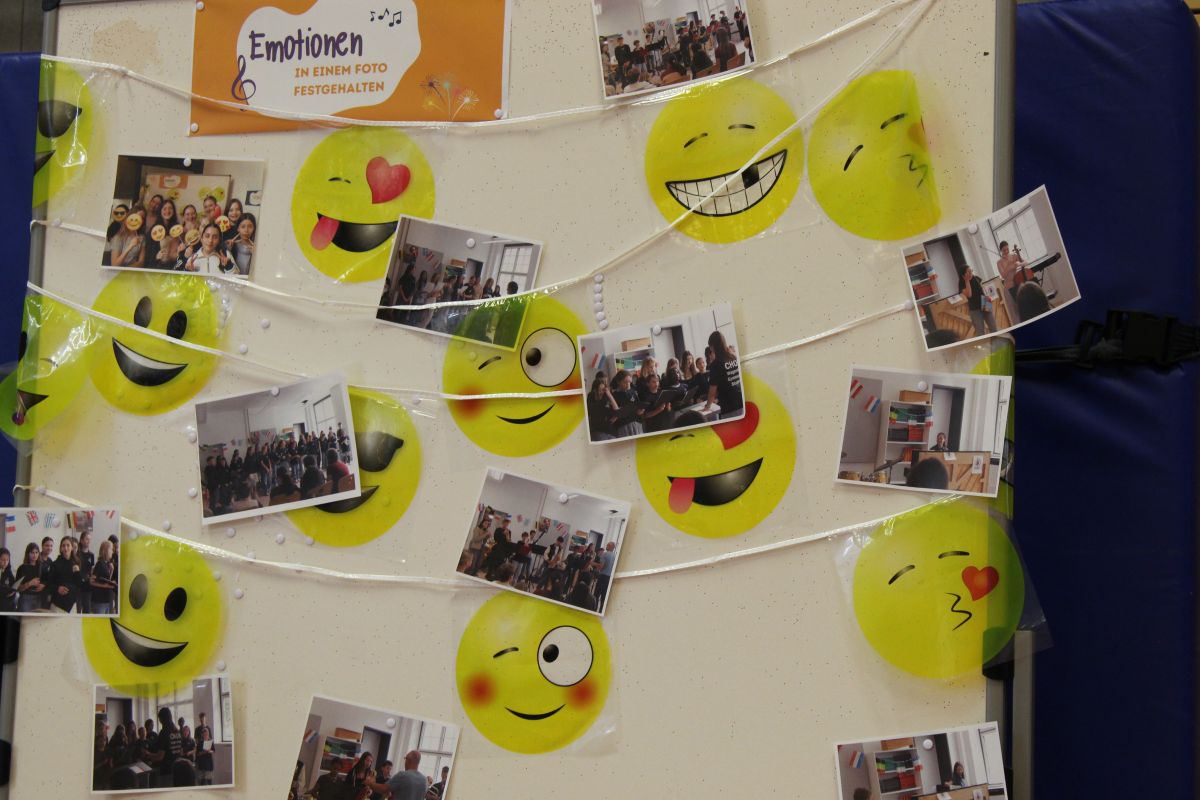 Mehrere Fotos von Gruppen und gelbe Smileys auf einer Pinnwand.