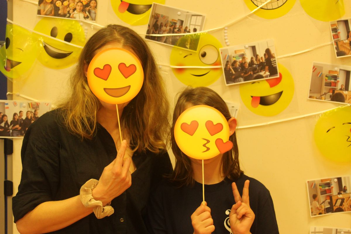 Zwei Personen mit Herzaugen- und Kuss-Emoji-Masken, posieren vor gelbem Smiley-Hintergrund.