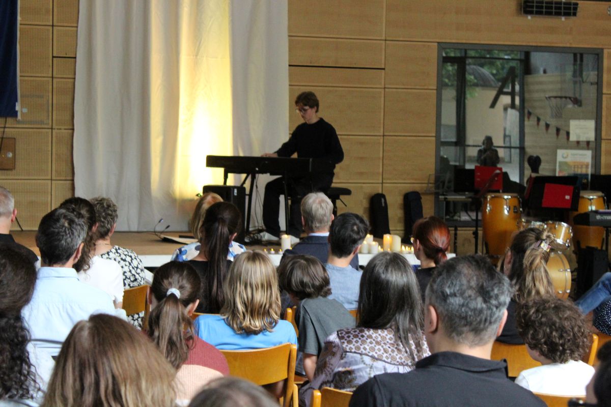 Eine Person spielt Klavier vor einem Publikum in einem Saal mit Holzwänden.