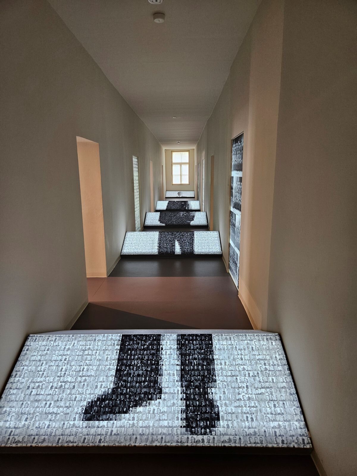 Flur mit leuchtenden Bodenbildern in Schwarzweiß. Fenster am Ende. Kunstvolle Beleuchtung.