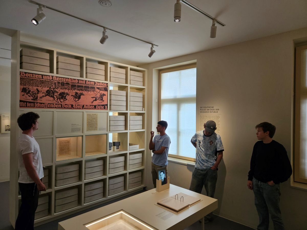 Vier junge Männer betrachten eine historische Ausstellungswand in einem lichtdurchfluteten Raum.