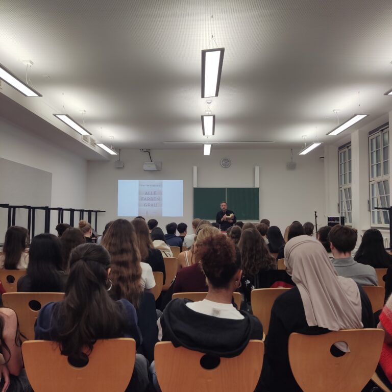 Eine Person spricht vor einem interessierten Publikum in einem Klassenzimmer.