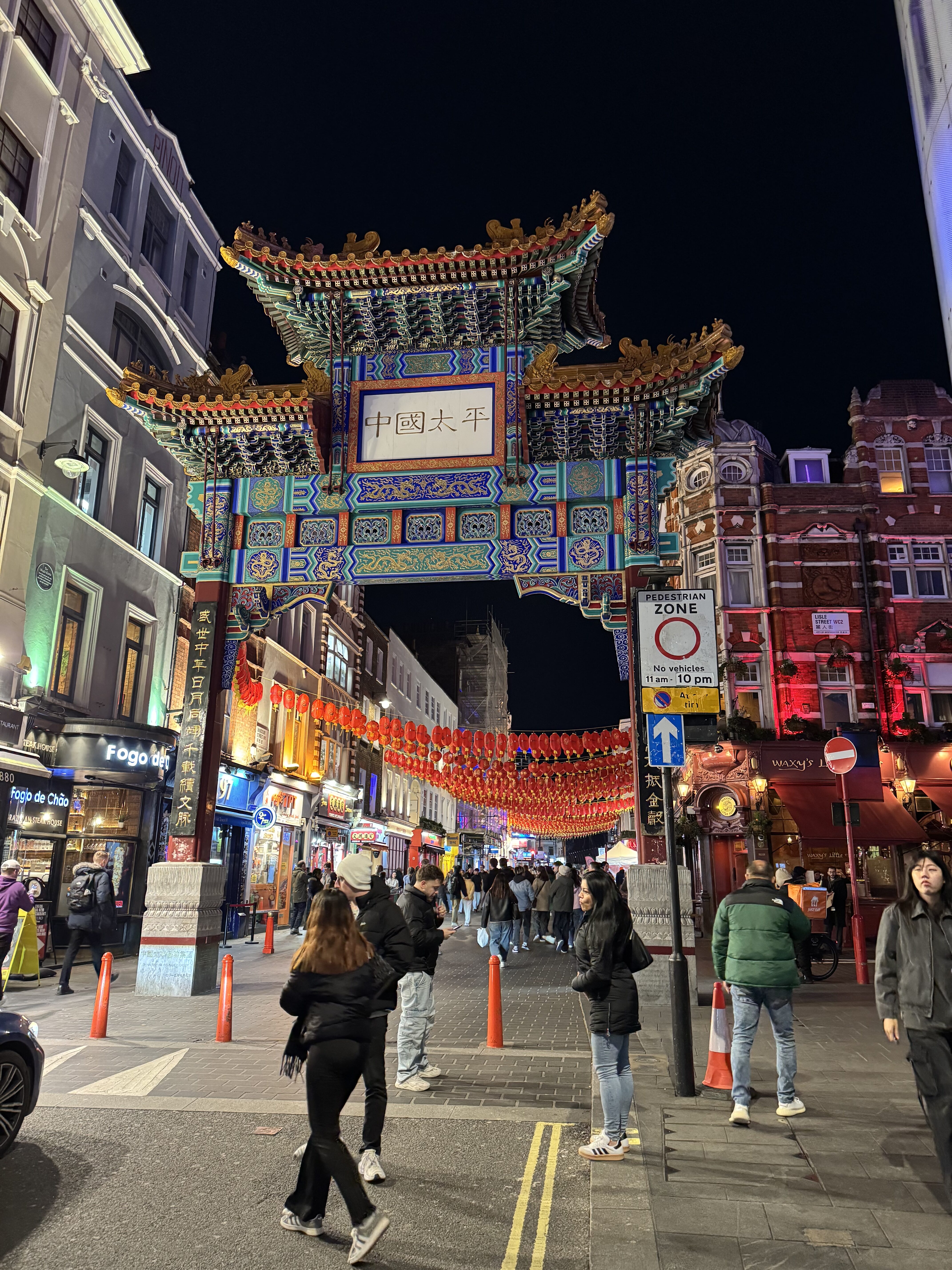 Traditionelles chinesisches Tor bei Nacht, Menschen spazieren belebte Straße.