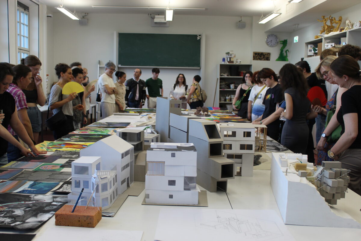 Eine Gruppe von Menschen betrachtet Architekturmodelle in einem Klassenraum.