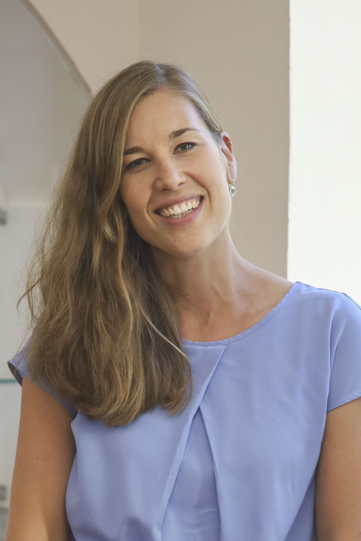 Eine lächelnde Frau mit langen braunen Haaren und einem blauen Oberteil