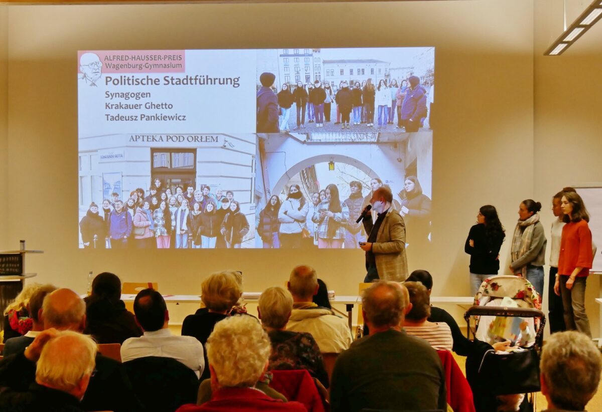 Eine Frau mit Mikrofon präsentiert vor Publikum Fotos einer Stadtführung auf einer Leinwand