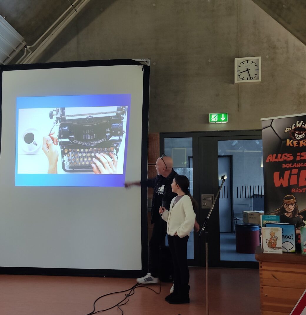 Ein Mann mit Brille und ein Kind zeigen lächelnd auf ein Bild einer Schreibmaschine