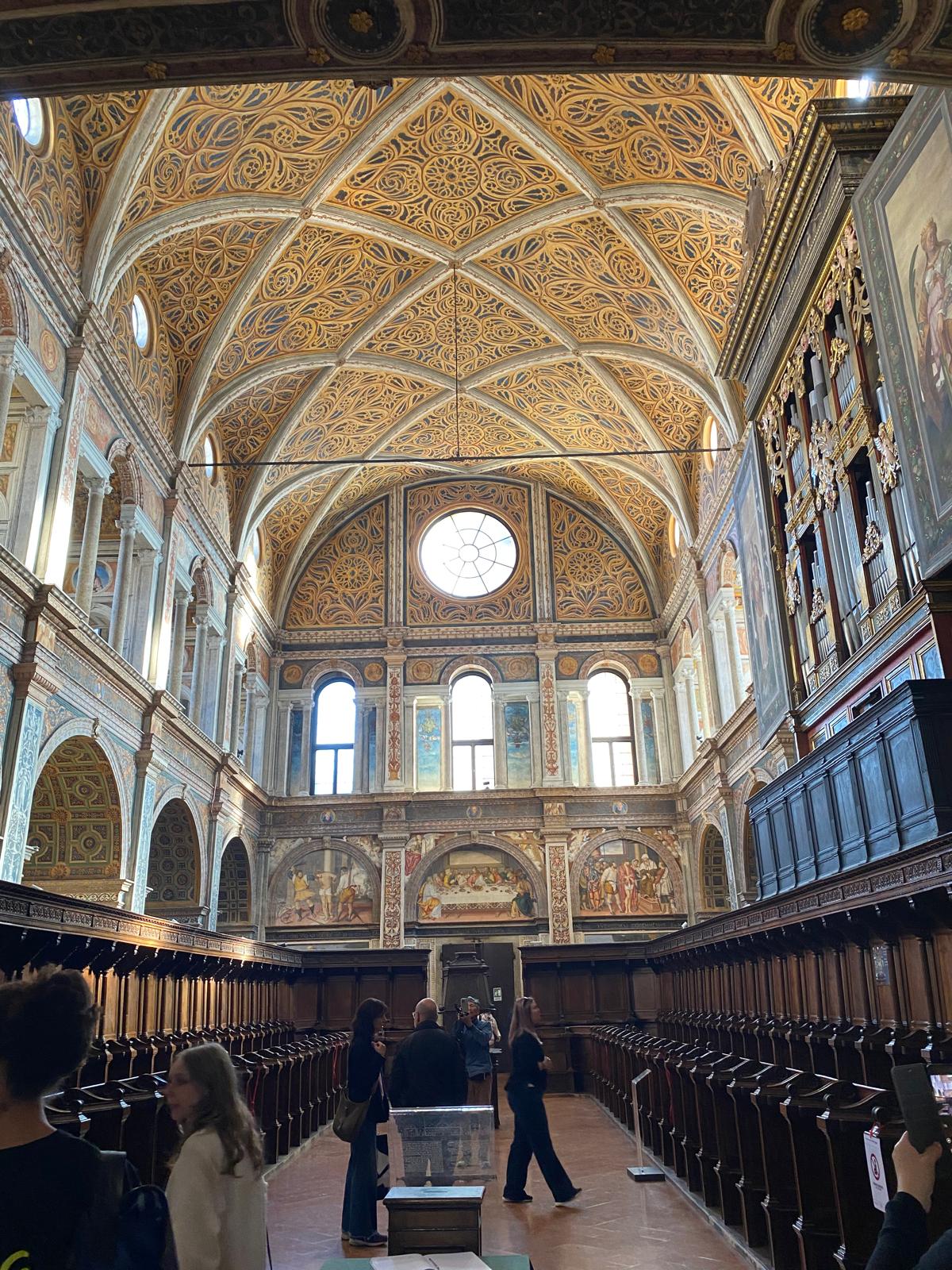 Mehrere Personen stehen unter einer aufwendig verzierten goldenen Decke in einer historischen Halle