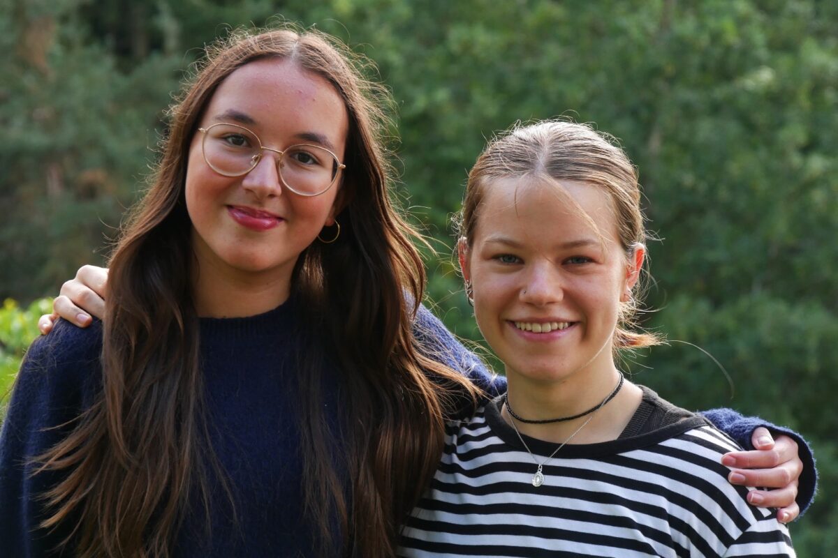 Zwei junge Frauen lächeln freundlich nebeneinander vor grünem Naturhintergrund
