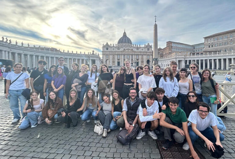 Eine große Gruppe junger Erwachsener lächelt fröhlich vor dem Petersdom in Rom