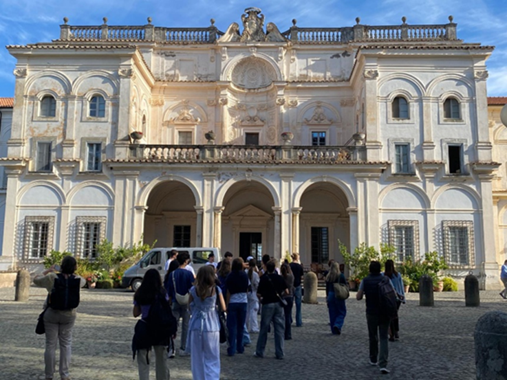Eine Gruppe Erwachsener steht vor einem hellen barocken Gebäude mit Verzierungen und Säulen