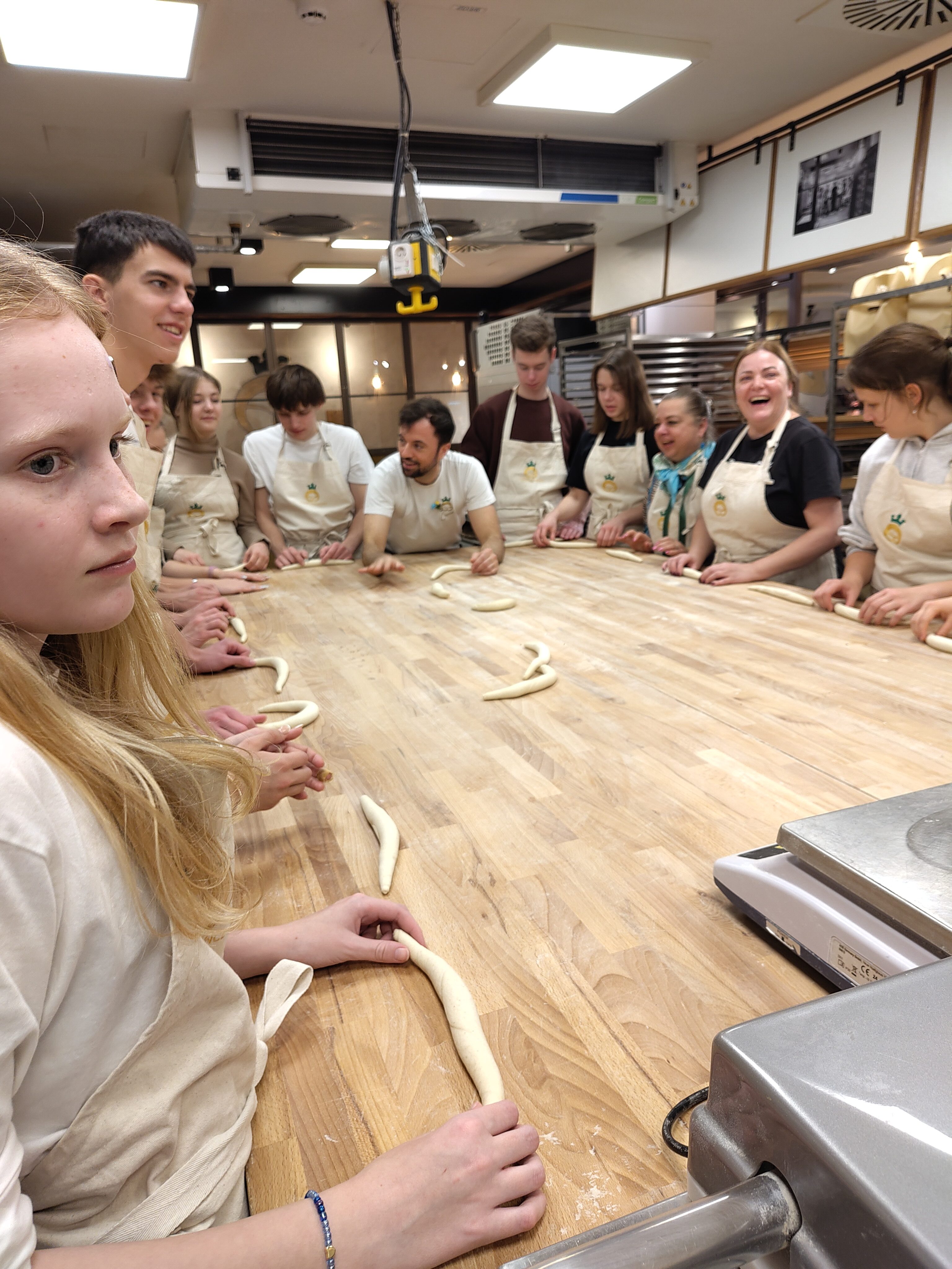 Junge Menschen in heller Kleidung rollen weißen Teig auf einem Holztisch und lachen