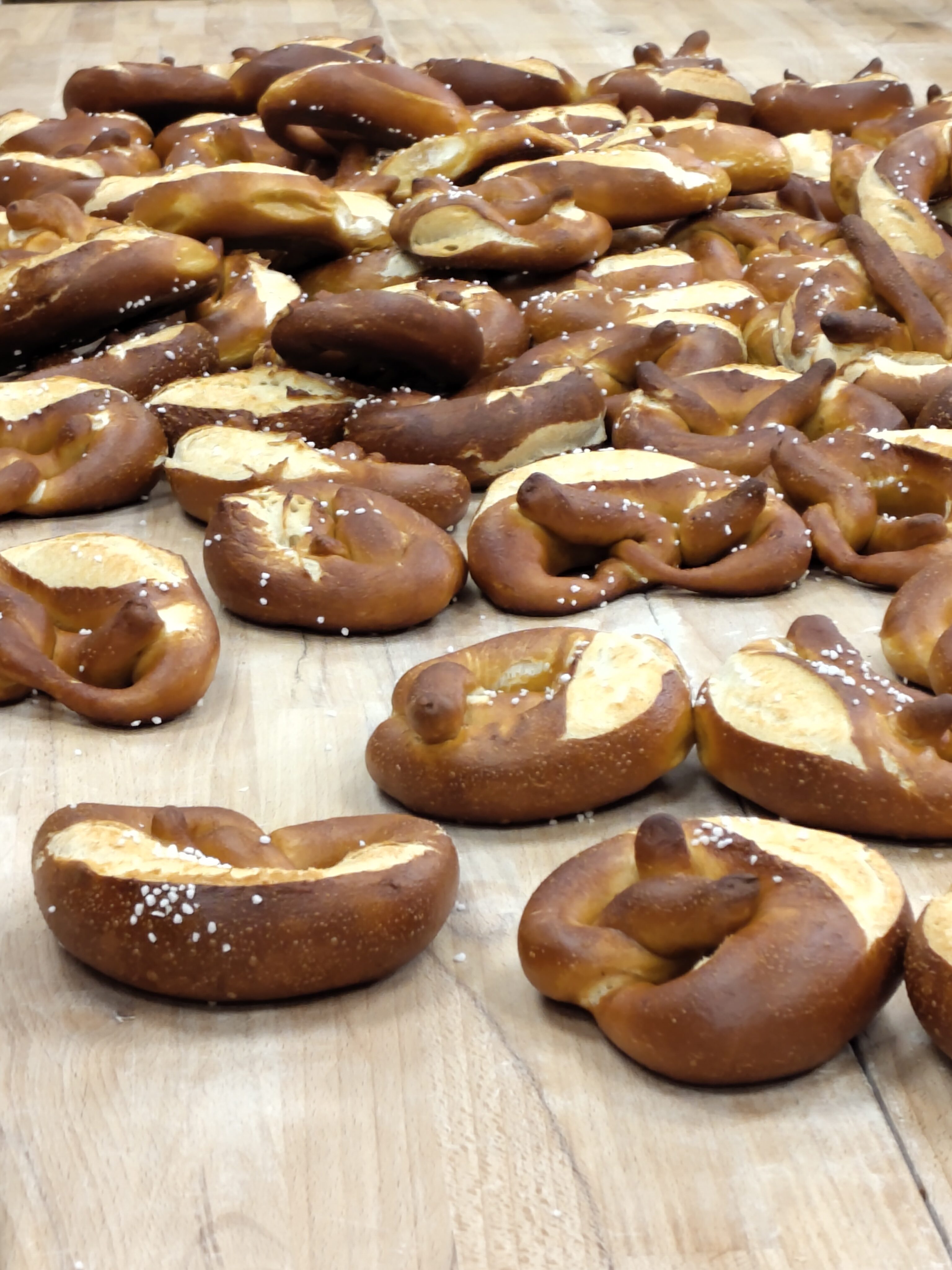 Viele goldbraune Brezeln liegen auf einem Holzbrett und sind mit grobem Salz bestreut