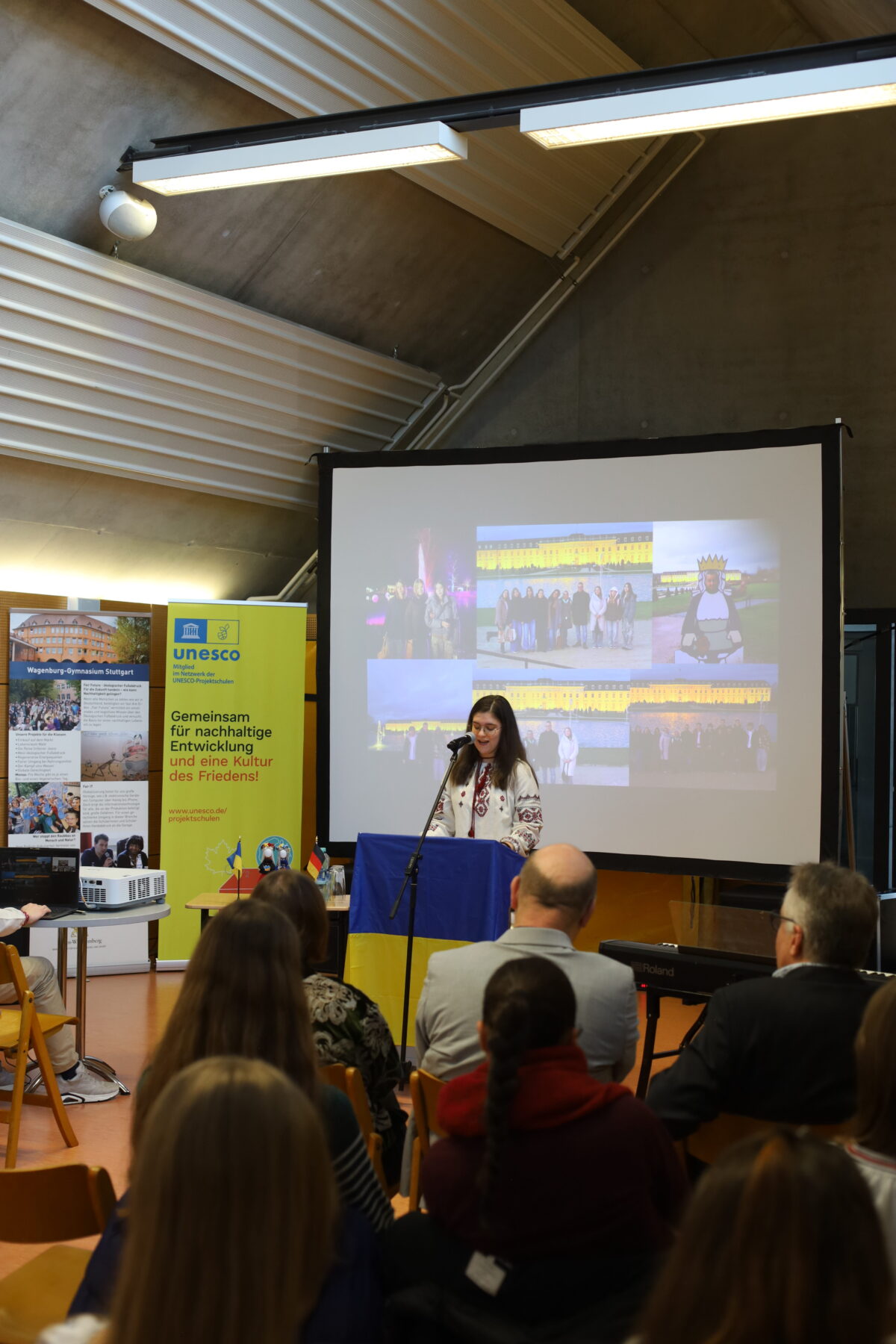 Eine Frau mit langen dunklen Haaren spricht lächelnd am Rednerpult vor Publikum