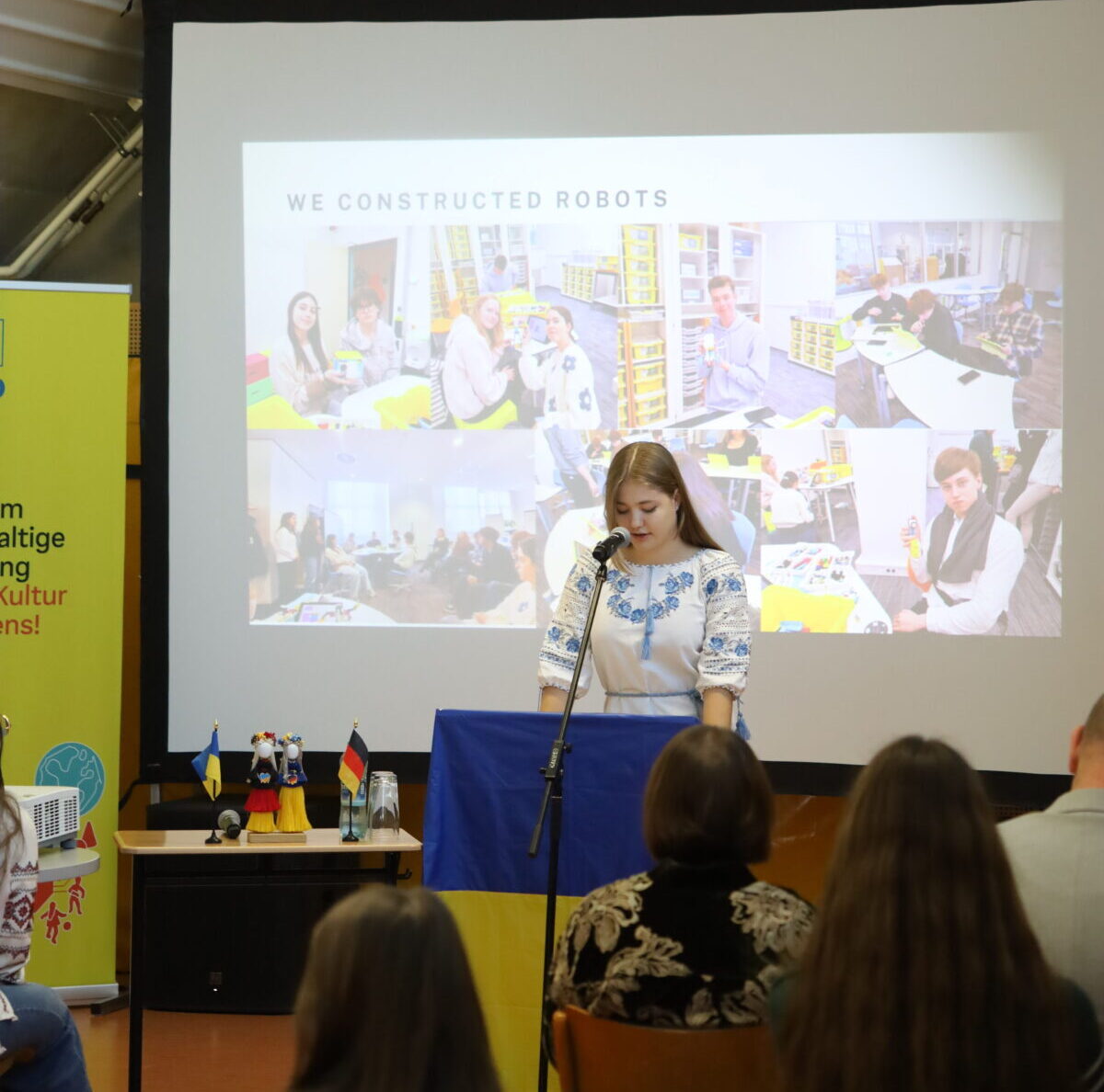 Junge Frau mit konzentriertem Blick steht an einem Rednerpult vor Publikum und Leinwand