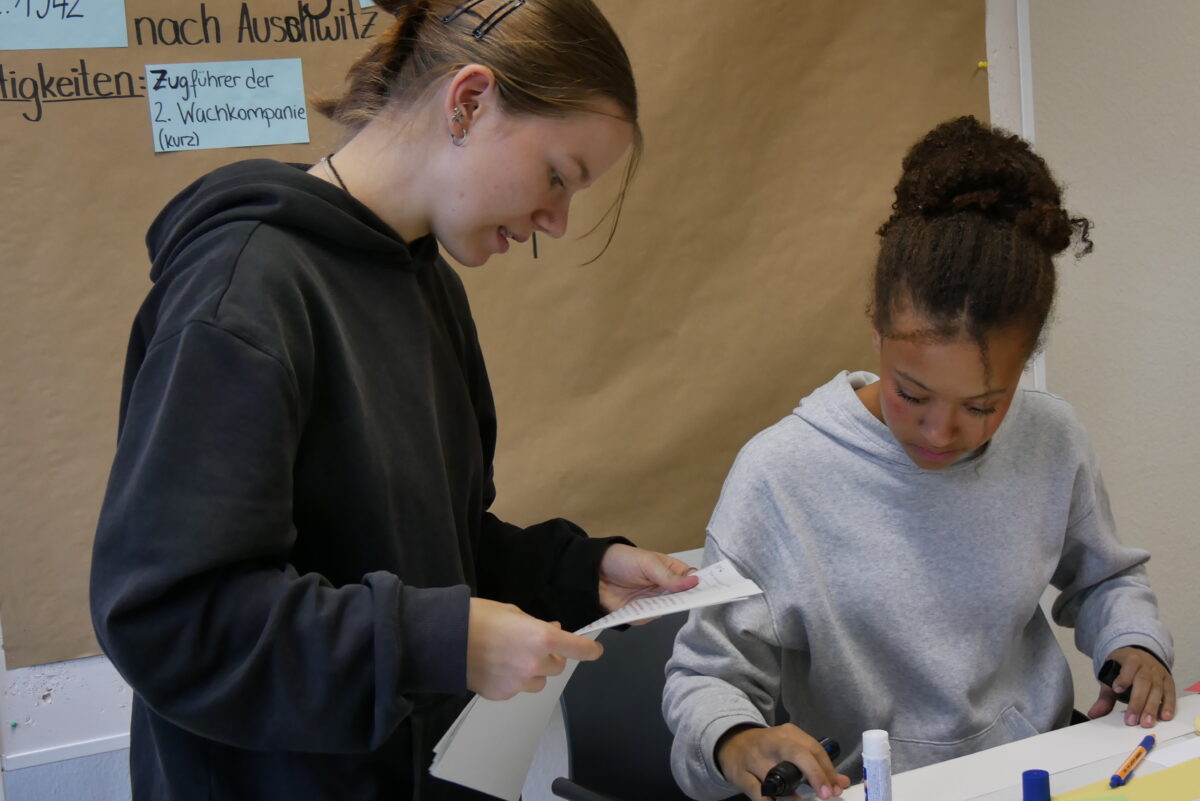 Zwei Jugendliche arbeiten konzentriert an einem Tisch mit Papier und Bastelmaterialien