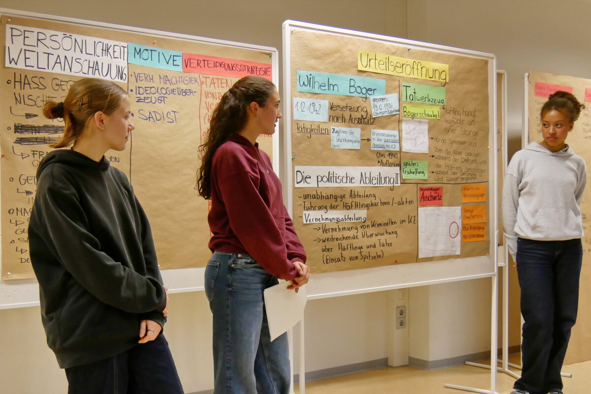 Drei junge Frauen stehen nachdenklich vor bunt beschrifteten Plakaten im Klassenraum