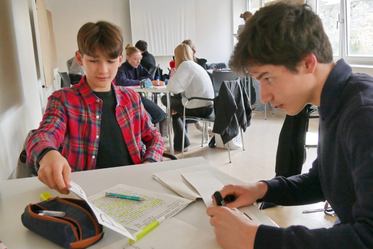 Zwei Jugendliche arbeiten konzentriert zusammen an einem Tisch mit bunten Textmarkern