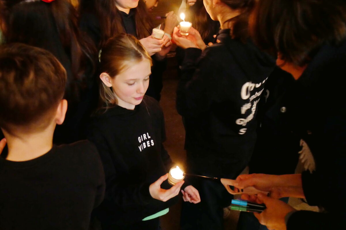 Ein blondes Mädchen mit ernstem Gesichtsausdruck hält eine brennende Kerze