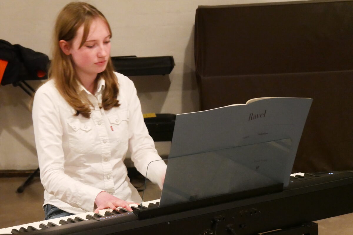 Junge Frau mit nachdenklichem Blick spielt konzentriert Klavier in hellem Raum