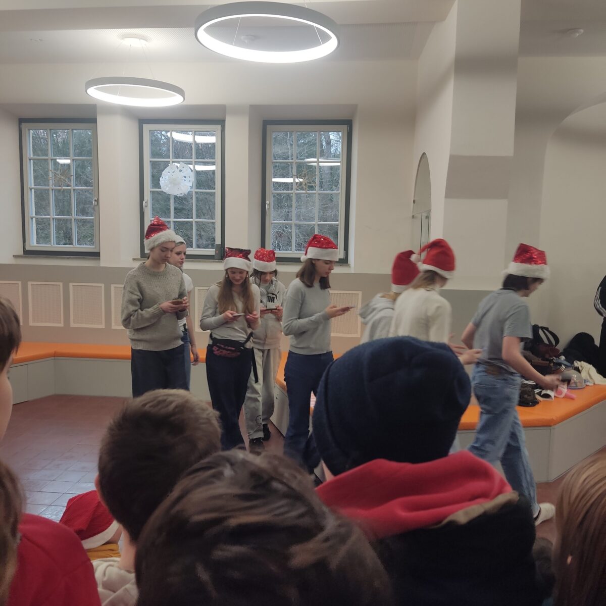 Mehrere junge Menschen mit Weihnachtsmützen wirken fröhlich und stehen vor einer Gruppe in einem hellen Raum