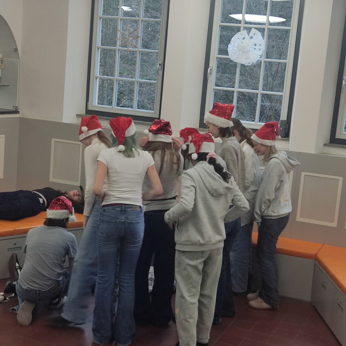 Eine Gruppe Jugendlicher mit roten Weihnachtsmützen schaut zu einer liegenden Person