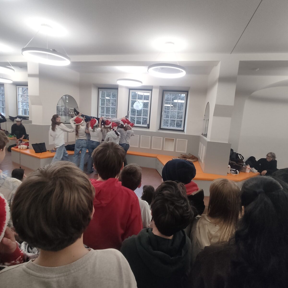 Eine Gruppe junger Menschen mit Weihnachtsmützen tanzt fröhlich vor zuschauendem Publikum