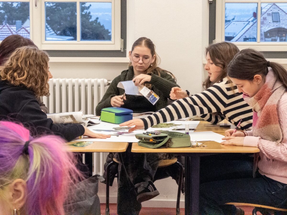 Vier junge Frauen mit konzentriertem Blick arbeiten gemeinsam an einem Tisch in einem Klassenraum