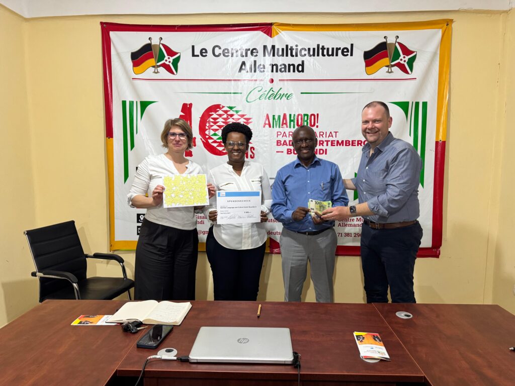 Vier Menschen stehen lächelnd vor einem Banner und halten Geschenke in den Händen