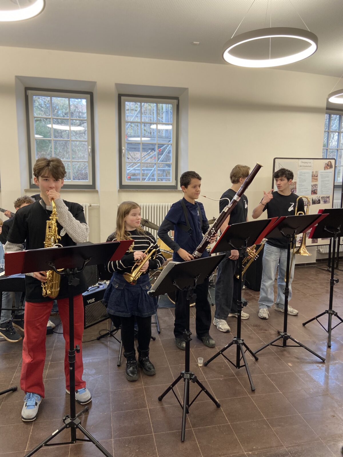 Fünf Jugendliche mit Blasinstrumenten stehen lächelnd in einem hellen Raum