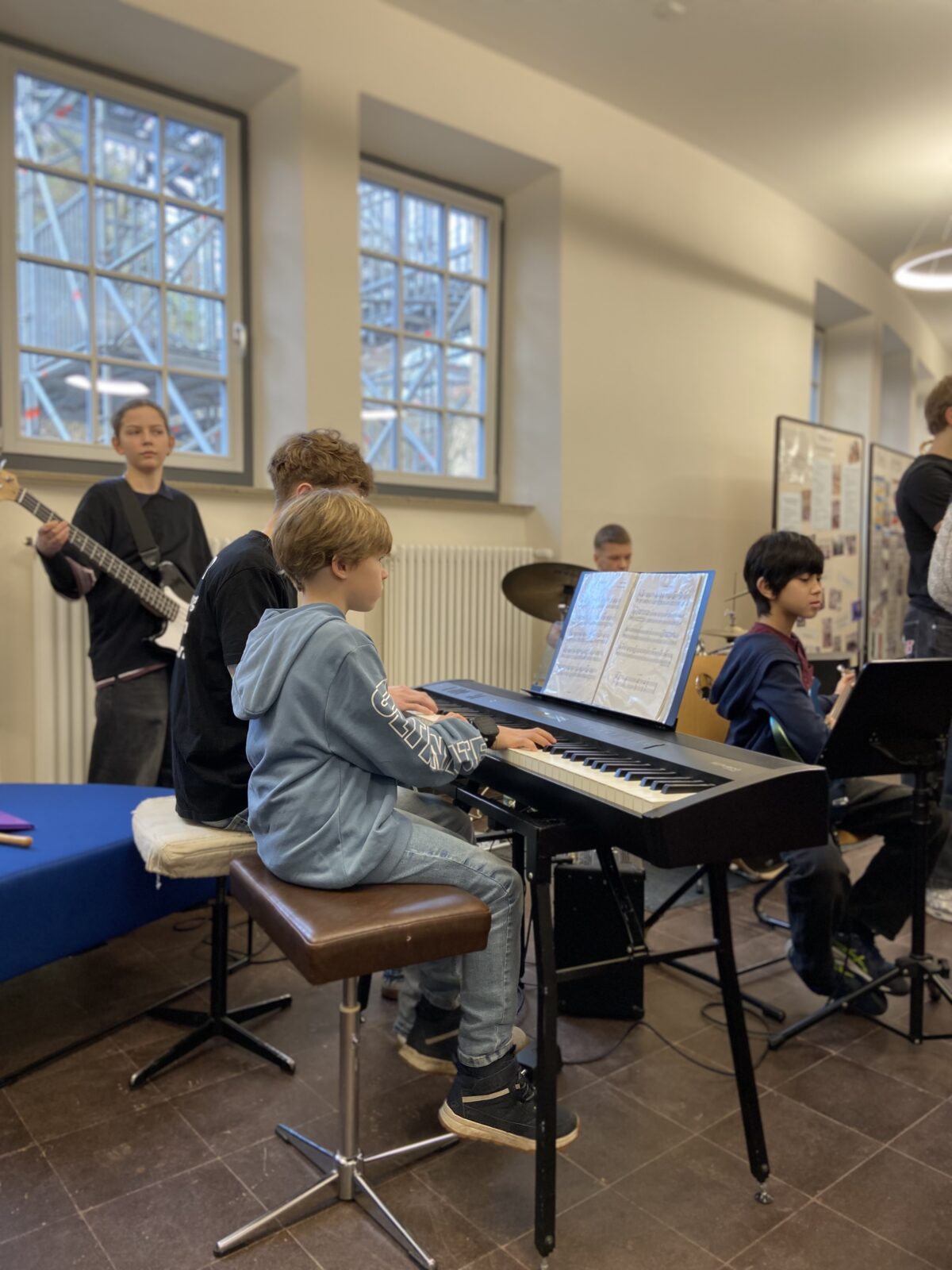 Ein Junge mit blonder Frisur spielt konzentriert Klavier neben einem älteren Jungen