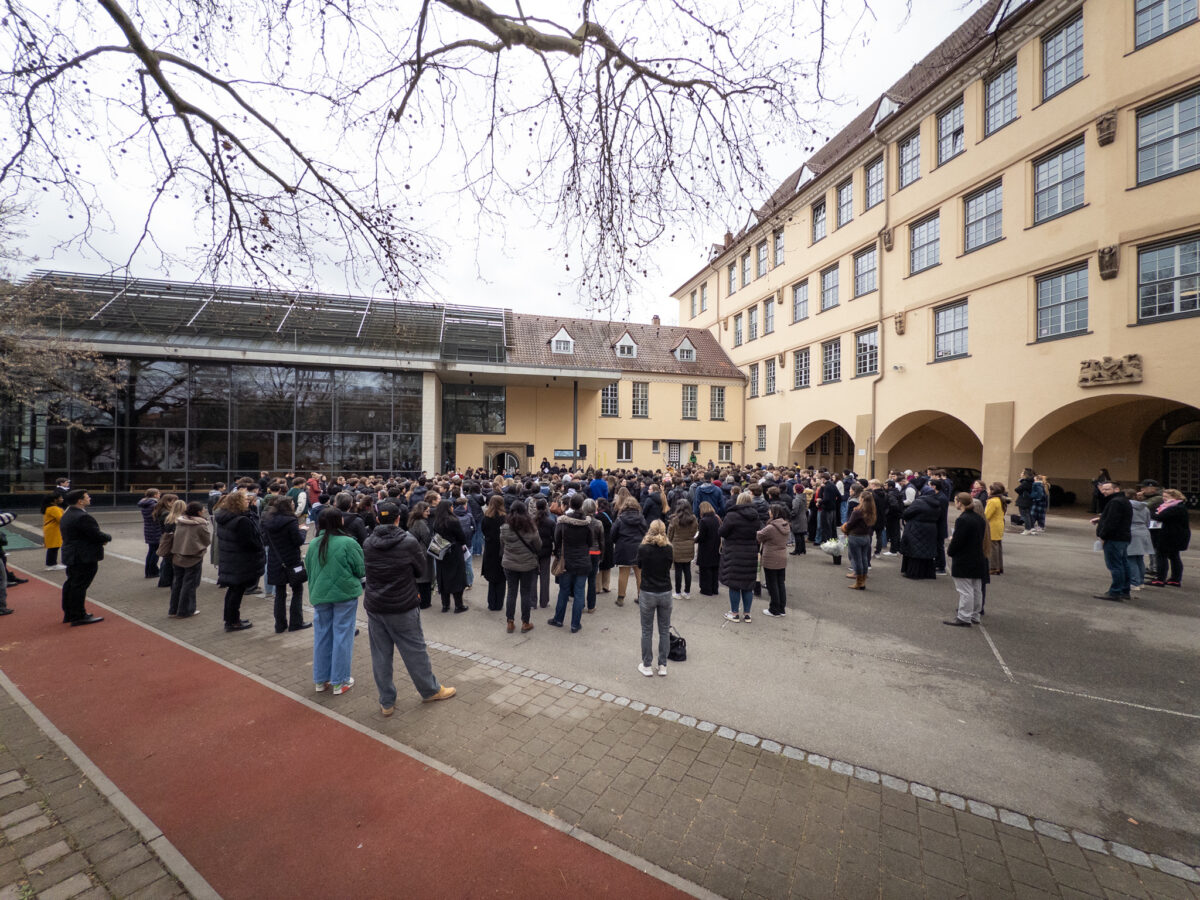 Viele Menschen versammeln sich auf einem Schulhof, einige mit winterlicher Kleidung