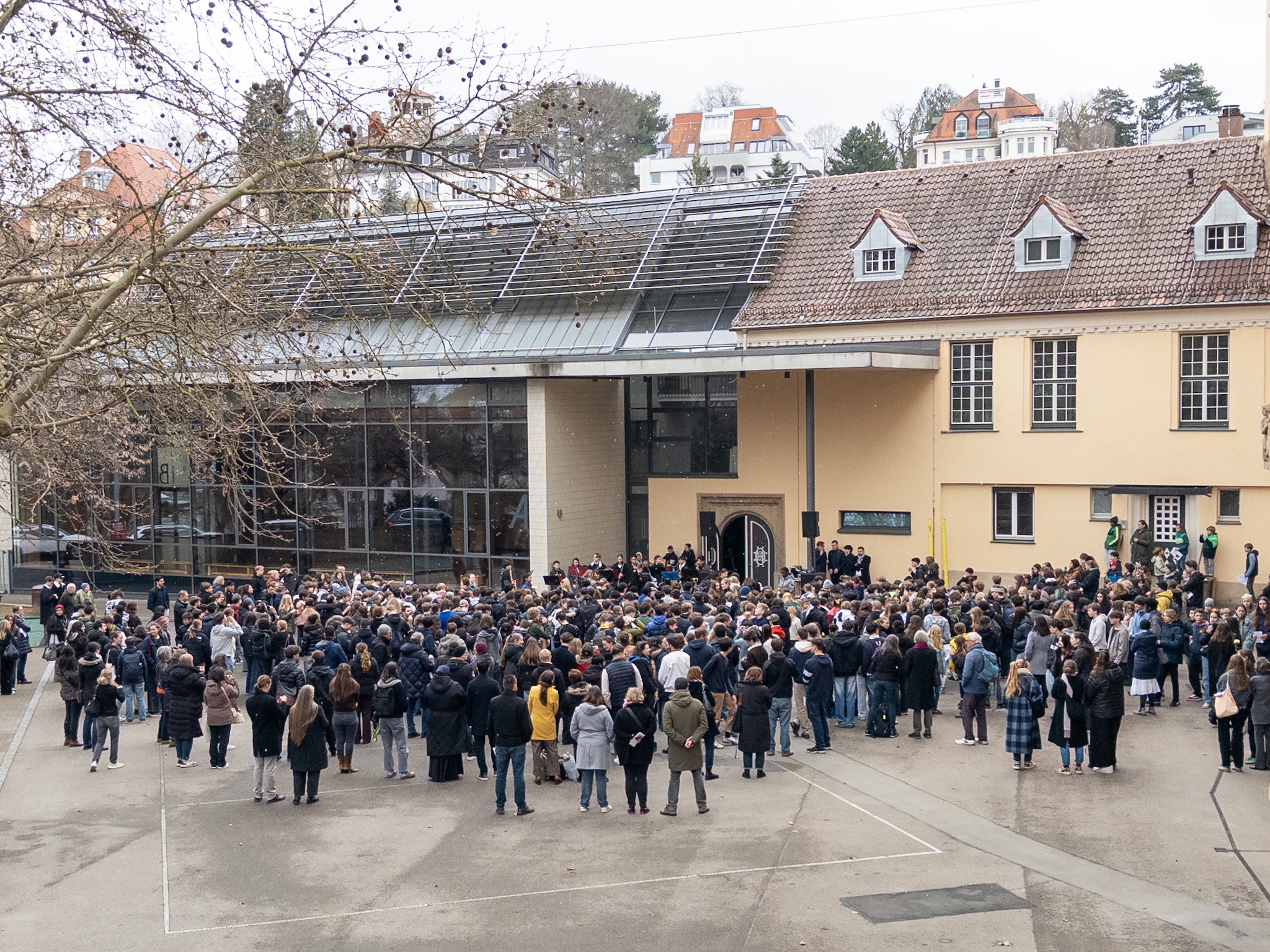 Viele Menschen versammeln sich vor einem gelben Gebäude bei bewölktem Wetter