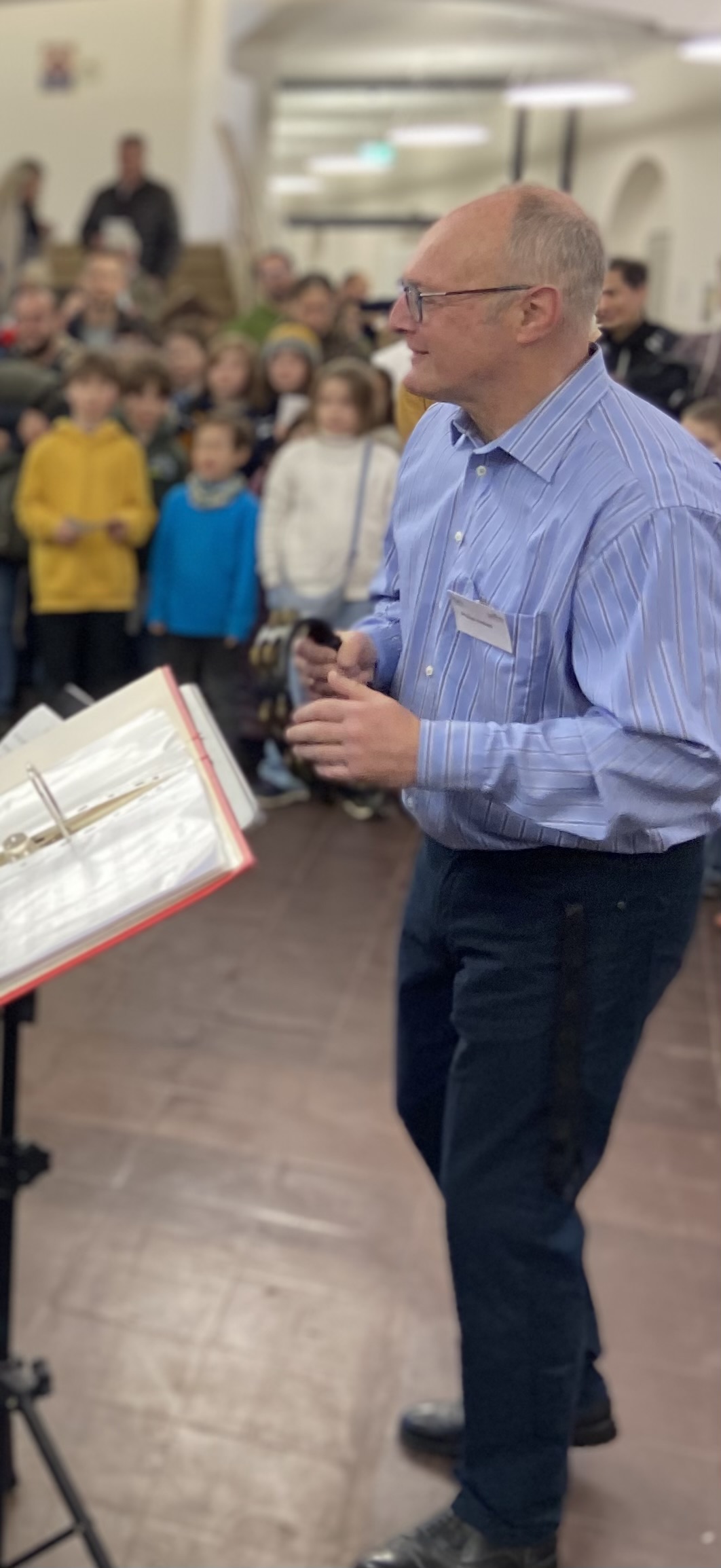 Ein älterer Mann mit Brille und blauem Hemd steht lächelnd vor einer Kindergruppe