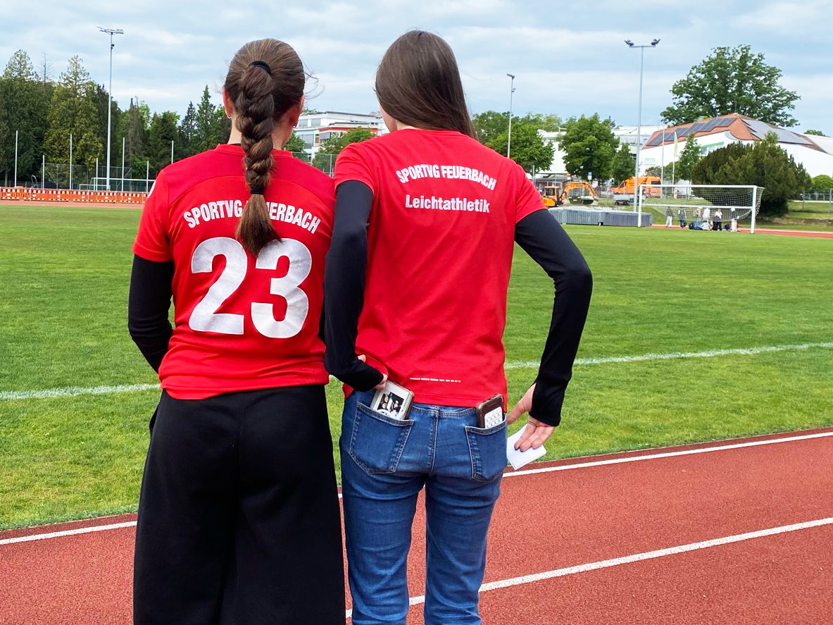 Zwei Frauen mit ernstem Blick in roten Sportshirts am Leichtathletikfeld
