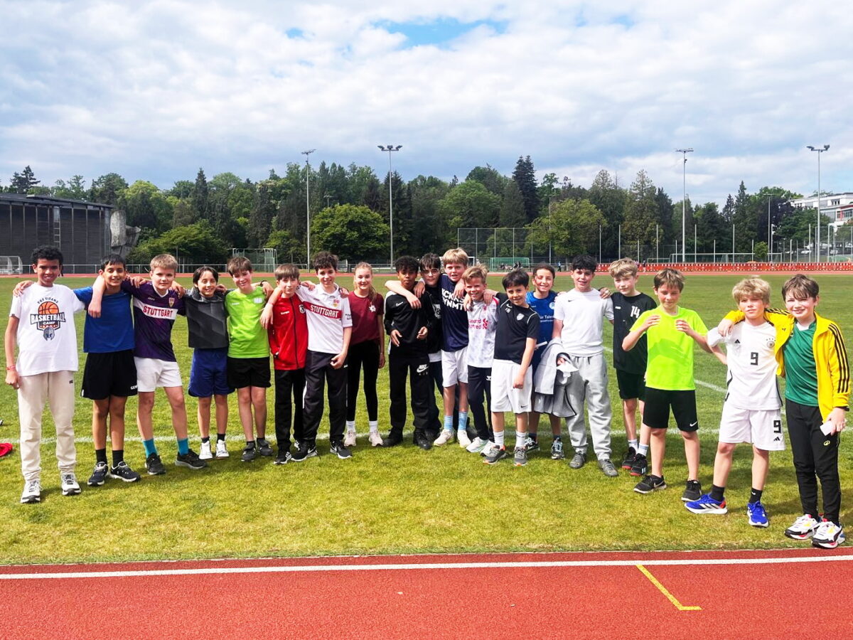Gruppe lachender Jungen in bunten Sportoutfits auf gruenem Sportplatz