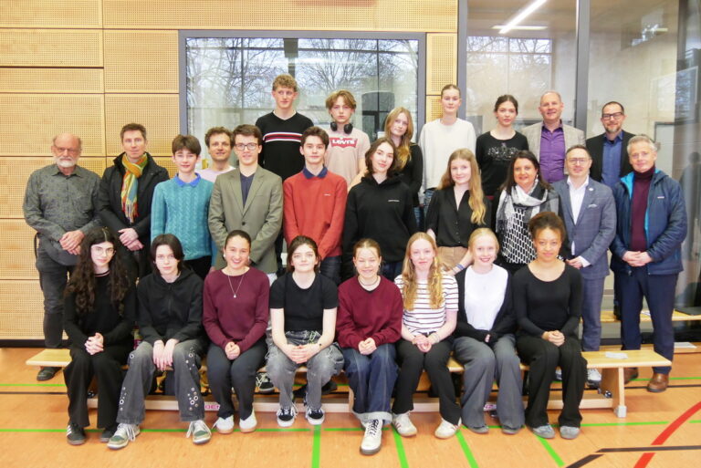 Gruppenfoto mit neutralen Gesichtern, bunte Kleidung, Sporthalle im Hintergrund