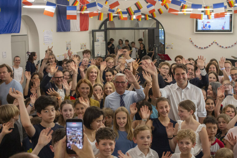 Laechelnde Menschenmenge winkt, bunte Flaggen und Handyaufnahme im Saal
