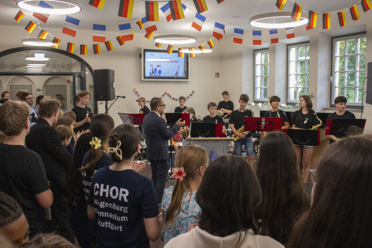 Jugendliche mit konzentriertem Blick musizieren vor Publikum, bunte Flaggen im Saal