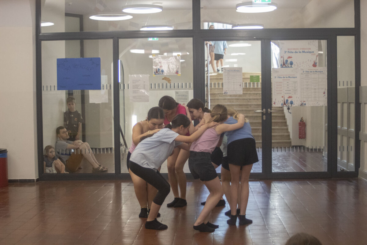 Gruppe Jugendlicher konzentriert in bunter Sportkleidung im Kreis hockend und umarmend