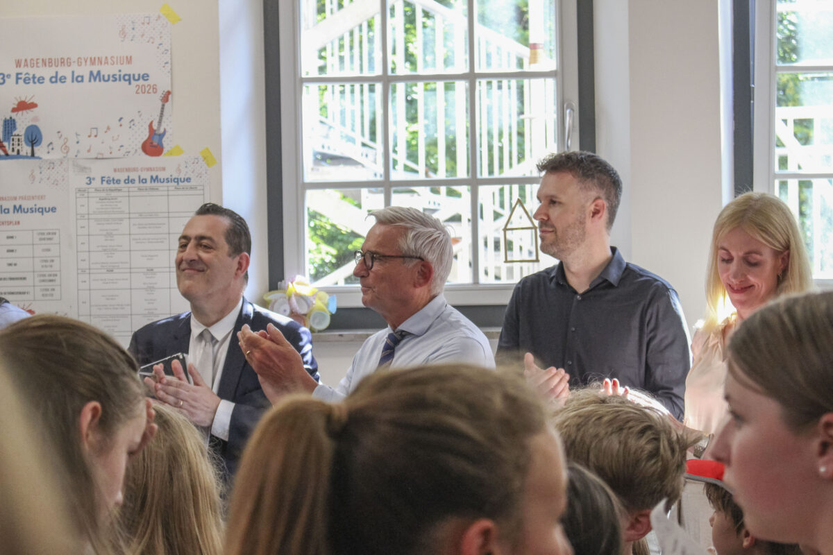Applaudierende Personen mit neutralem Ausdruck in heller Aula mit Plakat