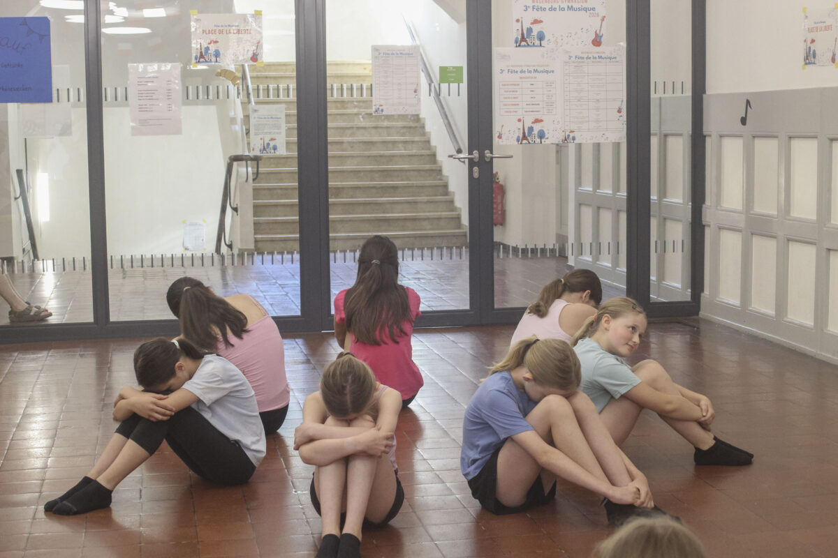 Traurige Kinder in bunten Shirts sitzen zusammengekauert in einer Halle
