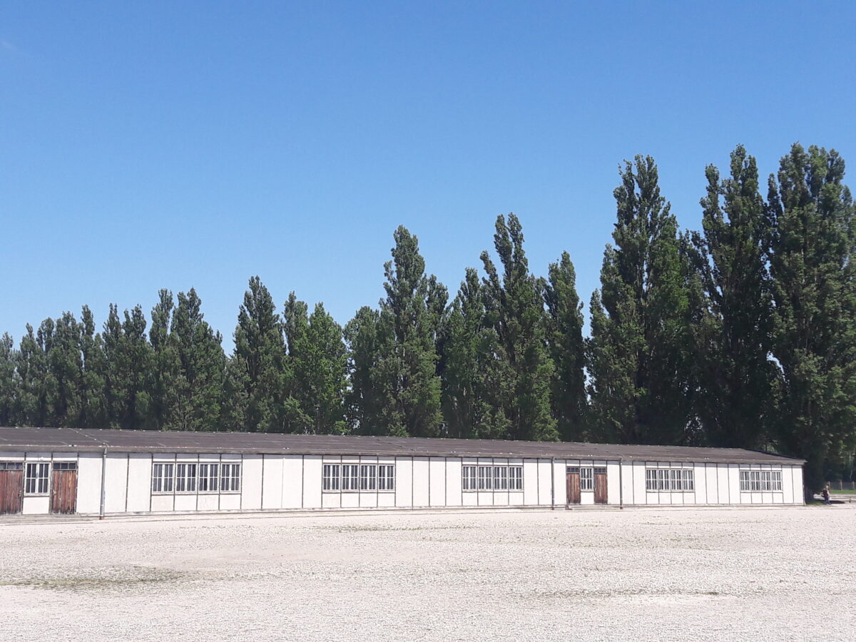 Langes weißes Gebäude vor grünen Bäumen unter blauem Himmel ohne Personen