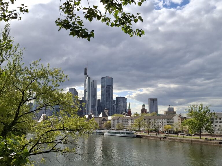 Blick auf Frankfurter Skyline am Main mit grünen Bäumen und Wolkenhimmel