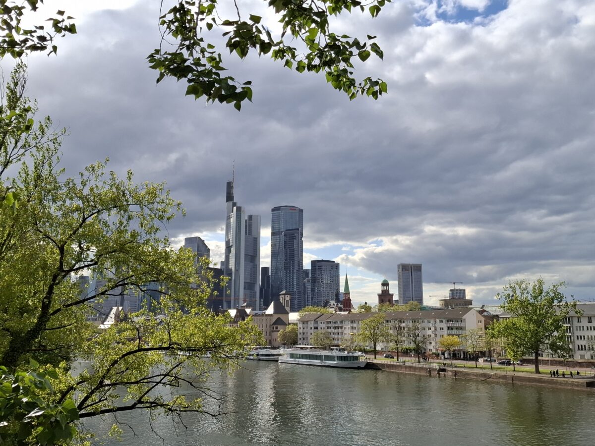 Blick auf Frankfurter Skyline am Main mit grünen Bäumen und Wolkenhimmel