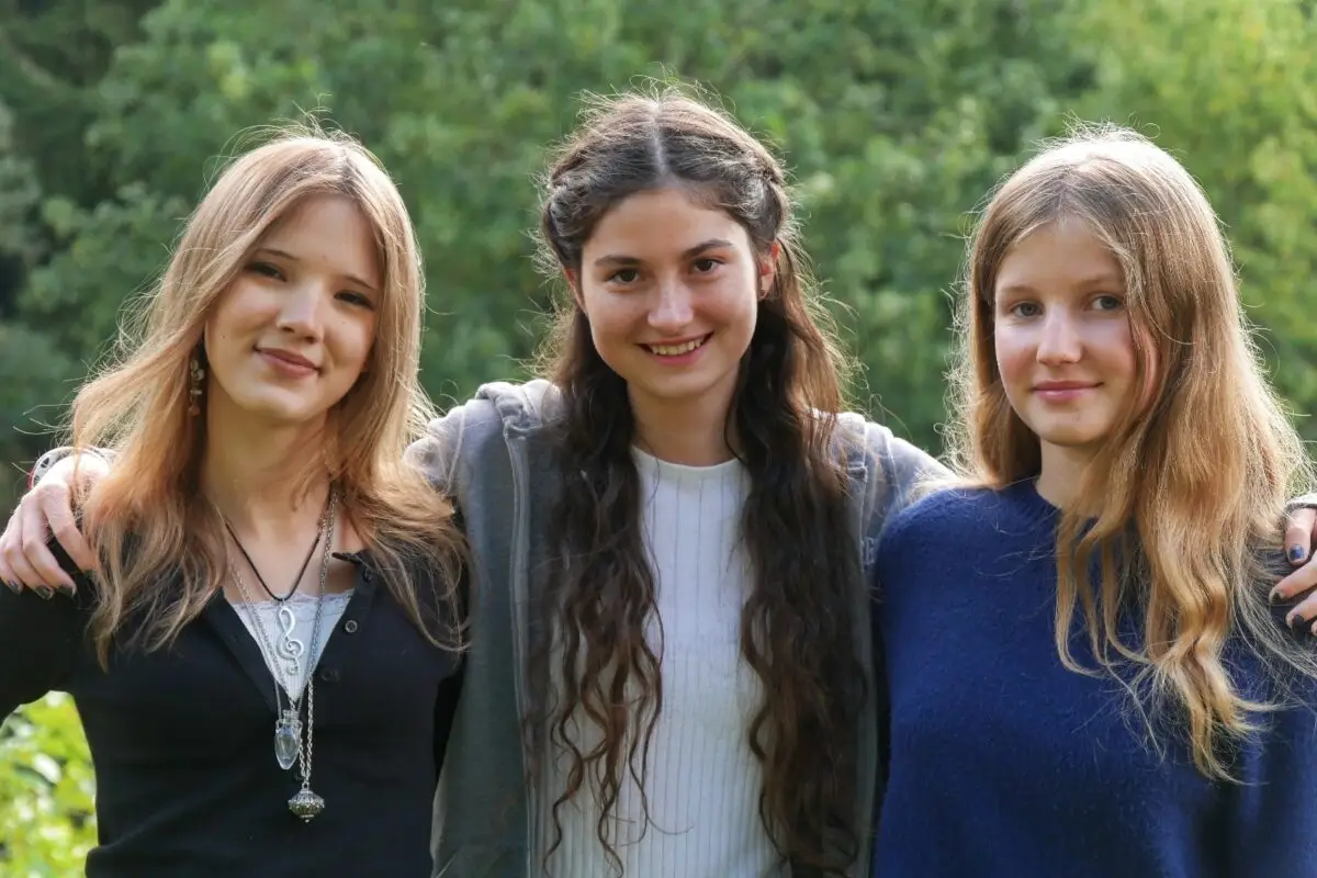 Drei lächelnde junge Frauen in Blau und Schwarz mit langen Haaren im Grünen
